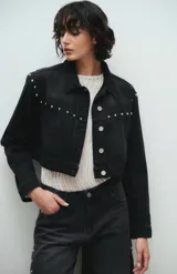 Campera de jean negra, corte crop, con cuello clásico, cierre frontal con botones metálicos y tachas plateadas en hombros y solapas.