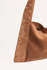Cartera tipo tote de gamuza color tostado, con diseño triangular y correas integradas decoradas con tachas metálicas doradas a lo largo de los bordes.