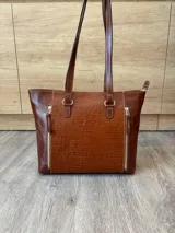Cartera de cuero vacuno color marrón, de diseño amplio con paneles combinados de diferentes texturas y un panel central con relieve de cocodrilo. Cuenta con cierre frontal vertical y asas de hombro.