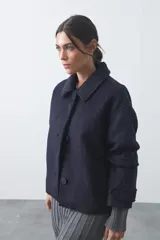 Tapado corto de paño con textura, color marrón, de corte recto y silueta estructurada. Presenta cuello camisero, cierre frontal con botones grandes y mangas largas con detalle de trabas en los puños.