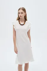 Vestido midi de poliéster color blanco, de corte recto y escote redondo a la base, con mangas cortas abuchonadas con volados y detalles de volados en el ruedo.