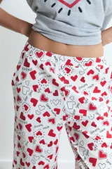 Pijama compuesto por una remera gris de manga corta con estampa frontal de corazón y un pantalón largo blanco con estampado de corazones rojos.