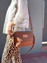 Cartera tipo bandolera de cuero color tostado, con solapa frontal, cierre principal y herrajes metálicos. Incluye dos correas desmontables, una corta para llevar al hombro y una larga ajustable para usar cruzada.