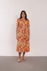 Vestido midi con estampado de círculos concéntricos en tonos naranja, amarillo y blanco. Tiene cuello camisero, mangas cortas y cinturón de la misma tela.