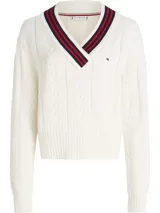 Sweater de punto color blanco hueso, con tejido trenzado (cableado) en el cuerpo y mangas. Presenta un cuello en V con ribete de rayas rojas y negras.