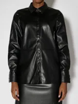 Camisa negra de manga larga con efecto cuero y acabado brillante. Presenta cuello clásico, cierre frontal de botones y puños abotonados. El diseño incluye un ligero volumen en las mangas.