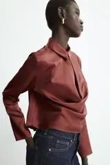 Blusa de tejido satinado con cuello solapa, manga larga y detalle de abertura drapeada en el pecho. Cierre frontal con botón forrado.