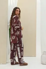Camisa de manga larga color marrón oscuro con estampado gráfico en color blanco de símbolos abstractos, ojos y soles. Posee cuello camisero y cierre frontal con botones.