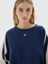 Buzo de felpa suave color azul marino con interior de frisa, calce oversized y detalles laterales a contratono en color beige en las mangas. Tiene un bordado del logo de la marca en el pecho y la palabra "PASTICHE" bordada en la espalda.