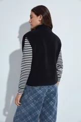 Chaleco de corderito negro con textura suave, cuello alto y cierre frontal completo. Cuenta con bolsillos laterales amplios y un diseño de calce relajado.