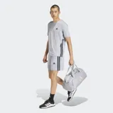 Remera deportiva Adidas de manga corta, color gris claro, con cuello redondo y diseño de las tres rayas características de la marca en color negro sobre los laterales. Presenta el logo de la marca en el pecho.