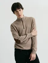 Sweater de punto color verde oliva, con cuello alto y medio cierre frontal. Presenta coderas en símil nappa y puños acanalados.
