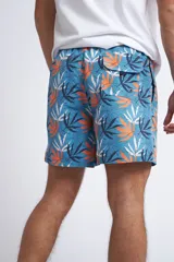 Short de baño con cintura elástica y cordón ajustable, confeccionado en tela ligera de secado rápido. Presenta un estampado botánico integral en tonos amarillos, blancos y azules, con dos bolsillos delanteros y uno posterior.