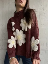 Sweater de punto color chocolate con diseño de flores grandes en relieve en color crema y centro amarillo. Presenta cuello alto, mangas largas y corte holgado.