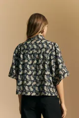 Camisa de manga corta con cuello camisero, confeccionada en tela estampada con diseño paisley en tonos negro, beige y azul.