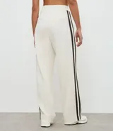 Pantalón deportivo de corte oversized estilo college, confeccionado en microfibra color crema con rayas laterales contrastantes en color marrón. Presenta cintura fija, bolsillos funcionales y frisos frontales.