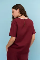Blusa de lino color beige, de corte recto y mangas cortas, con costuras decorativas pespunteadas en tono rojizo que forman líneas verticales y horizontales.