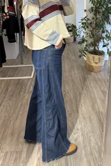 Pantalón de jean azul oscuro con corte wide leg, tiro alto y costuras verticales decorativas en el frente. Presenta un ruedo desflecado y un diseño de pierna ancha.