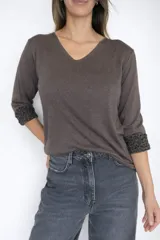 Sweater de tejido de punto color gris, con escote en V y mangas largas. Presenta un diseño liso en el exterior y un detalle de animal print en el interior de los puños, visible al doblarlos.