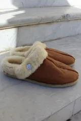 Pantufla de cuero color habano con interior de piel sintética, suela de goma y detalle de costura central.