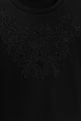 Camiseta de algodón color negro, con cuello redondo y manga corta. Presenta un detalle de bordado floral al tono en la parte frontal.