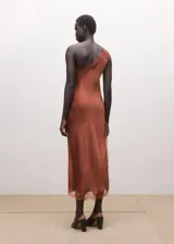 Vestido midi asimétrico de tejido satinado en color tostado, con un tirante fino y otro hombro descubierto. Cuenta con delicados ribetes de encaje a tono en el escote y en el bajo, y una sutil abertura lateral.