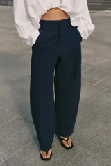Pantalón barrel color azul marino, de tiro bajo, pernera holgada con diseño redondeado que se estrecha hacia el tobillo, con bolsillos delanteros y cierre frontal.