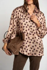 Camisa oversize de poliéster color rosa con estampado de lunares marrón oscuro, cuello camisero, cierre frontal de botones y mangas largas con puños elásticos.