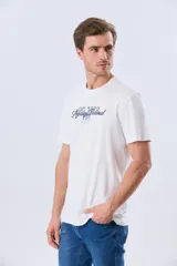 Remera azul marino de manga corta con cuello redondo, confeccionada en mezcla de algodón y poliéster. Presenta un diseño en el frente que combina estampa y bordado con la leyenda "Legacy Brand 1972" en tonos rosado, verde y marrón.