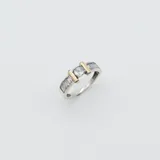 Anillo de plata 925 con detalles en oro, presenta un diseño central con una circonia redonda engastada entre dos barras doradas, flanqueada por circonias rectangulares en el cuerpo del anillo.