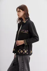Campera estilo militar (army) color negro, con calce recto y ajuste interno en la cintura mediante cordón con borlas. Presenta bordados con apliques de lentejuelas en el cuello, bolsillos frontales y puños.