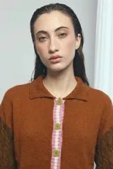 Cardigan de punto color marrón, con cuello vuelto, cierre frontal de botones y detalles de ribetes a rayas en los puños, la cintura y la botonera. Las mangas presentan un diseño tejido en relieve con textura de ochos.