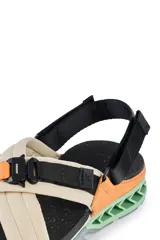 Sandalias Kenner Rakka Cross Craft con tiras cruzadas de tela color beige y ajuste con hebilla de plástico negra. Suela de goma negra con detalles en naranja y verde.