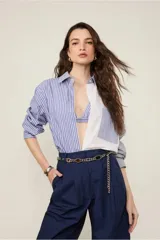 Camisa de tricoline con mezcla de rayas azules y blancas, cuello clásico, manga larga y bolsillo frontal, con cierre de botones y pliegue en la espalda. Incluye top que funciona como sobreposición.