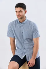 Camisa de manga corta confeccionada en mezcla de lino y algodón, con estampado de cuadros pequeños en tonos azules. Presenta cuello camisero con botones, cierre frontal abotonado, bolsillo aplicado en el pecho y dobladillo redondeado.