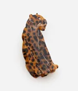 Pinza para el pelo con forma de leopardo en posición sentada, confeccionada en acetato con patrón de carey en tonos marrones y negros. Cuenta con detalles lineales grabados en color blanco.