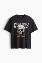 Remera negra de algodón de peso medio, corte holgado (Loose Fit), con cuello redondo. Estampado frontal con el logo de Guns N' Roses, una calavera con una rosa y una cadena, y el texto "Appetite for Destruction 1987-1988".