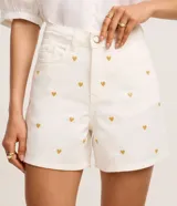 Short mom de cintura alta confeccionado en jeans color crudo, con bordado de corazones metalizados dorados, trabillas en la cintura, cierre tradicional y cinco bolsillos.