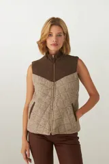 Chaleco corto de lana fina sin teñir, con diseño acolchado y pespuntes en forma de rombos. Presenta un canesú superior en color marrón oscuro y el cuerpo principal en tweed marrón claro con patrón de cuadros. Tiene cuello alto y cierre frontal con cremallera dorada.