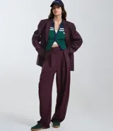 Pantalón de sastrería corte barrel, color marrón oscuro, con pliegues delanteros, cintura con cierre desplazado y piernas anchas.
