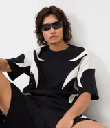 Remera boxy de algodón y poliéster color negro, con cuello redondo, manga corta y aplicaciones gráficas de llamas blancas en los laterales y las mangas.