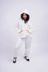 Conjunto deportivo compuesto por un buzo tipo hoodie con capucha y bolsillo canguro frontal, y un pantalón de jogging a juego. Ambas prendas son de color blanco y presentan un pequeño logo bordado en negro.