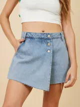 Short pollera de denim con diseño cruzado, cierre frontal con botones metálicos y ruedo deshilachado.