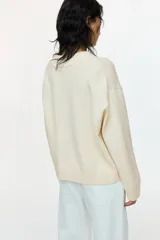 Buzo oversized de punto suave, color beige, con escote en V acanalado, hombros caídos y mangas largas. Cuenta con ribetes acanalados en los puños y en el dobladillo inferior.
