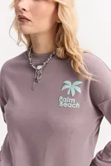 Buzo de algodón color lila, de calce relajado y hombros caídos, con estampa pequeña en el frente que dice "Palm Beach" y una palmera.