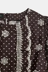 Blusa azul marino con estampado de lunares blancos, cuello redondo y mangas abullonadas. Presenta detalles de bordados perforados, volantes delanteros y acabados elásticos.