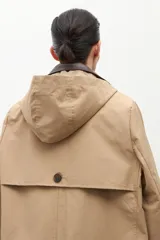 Trench impermeable color beige con cuello camisero en contraste de color marrón oscuro. Presenta cierre frontal con botones, bolsillos delanteros con solapa y mangas largas.