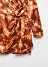 Vestido corto de manga larga con diseño drapeado y cruzado en la cintura. Presenta cuello redondo y un estampado tie-dye en tonos marrones y beige sobre un tejido satinado y fluido.