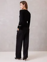 Buzo de tejido soft color negro, con cuello a la base y mangas largas. Presenta apliques de perlas decorativas en el contorno del cuello y en los puños.