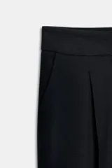 Pantalón tobillero de tiro alto con pliegues delanteros, bolsillos laterales y bajo con vuelta. Presenta cierre frontal con cremallera, botón y gancho.